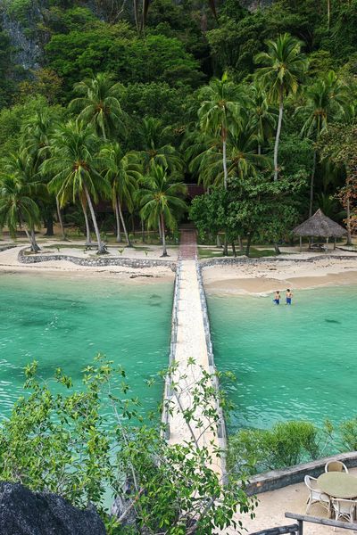 Stone jetty crossing a turquoise lagoon to a palm-lined beach