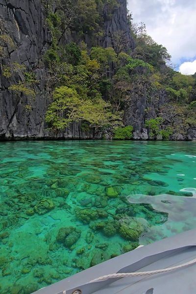 Clear turquoise water over coral beneath a limestone cliff, seen from the tender