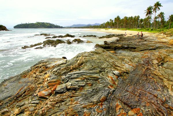 Layered rock shelf in Alimanguan with the coconut-lined sweep of Long Beach behind