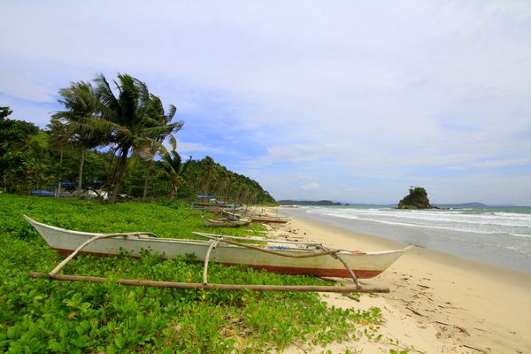 Outrigger bangka on the grass above Alimanguan Beach with a rocky islet offshore