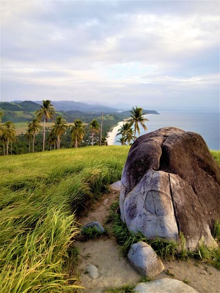 The Bato ni Ningning boulder on a grassy ridge above Irawan Beach and the coast
