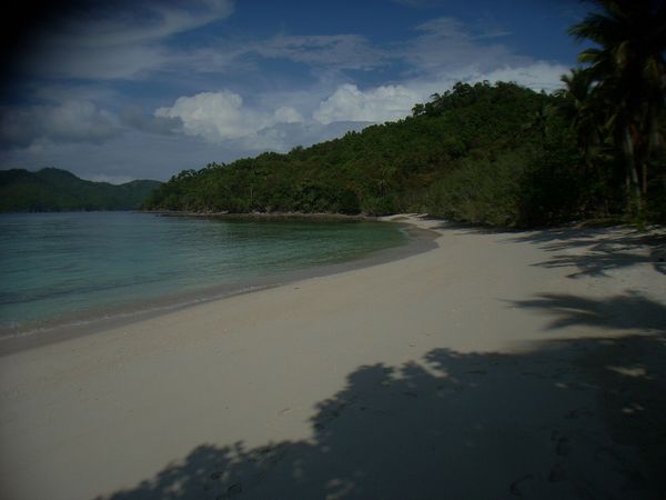 Empty curve of white sand below forested hills on Boayan Island