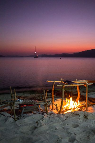 Beach barbecue and campfire at dusk with the yacht anchored offshore