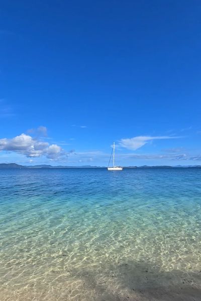 The yacht at anchor in clear shallow water off a sandy beach