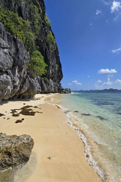 Sandy beach under dark limestone cliffs with clear water