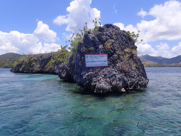 Rocky limestone islet at Siete Pecados Marine Park, Coron Bay, with the park's signboard mounted on the rock above clear shallow water