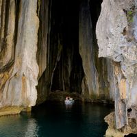 Tall limestone sea cave entrance at Cathedral Cave, Pinasil Island, El Nido, with a small dinghy floating inside