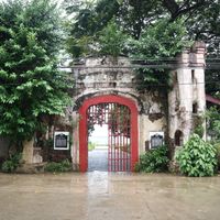 Weathered stone gateway of Plaza Cuartel with a red iron gate, historical markers set into the walls and the bay visible through the arch