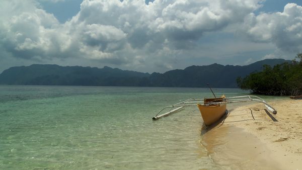 An outrigger bangka pulled up on the sand at CYC Island, Coron, with limestone ridges across the water