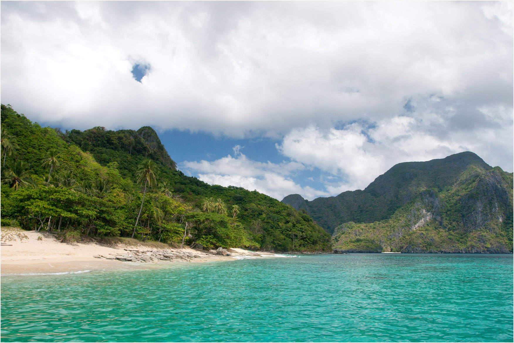 The beach on Helicopter Island, pale sand backed by palms and jungle with turquoise shallows in front